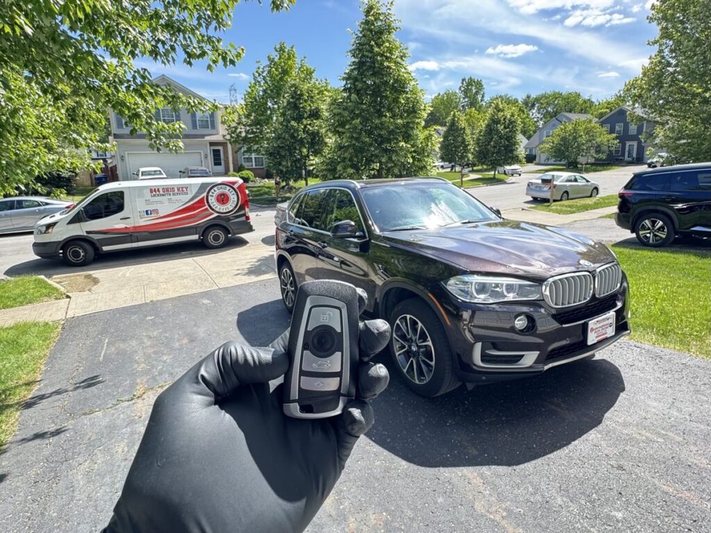 Automotive locksmith holding a new key for a 2015 BMW X5, with the customer’s car and service van behind